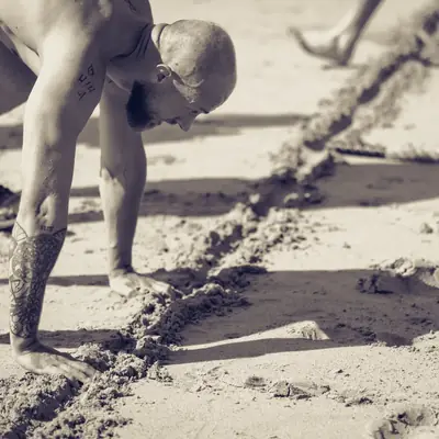 Sportif en effort sur le sable, mains dans la trace d’une corde